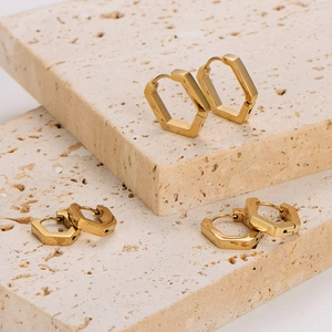 Three pairs of polished gold pentagon hoop earrings on minimalist beige stone decor