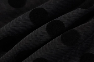 Macro detail of black polka dot fabric featuring velvet flocking and premium mesh texture