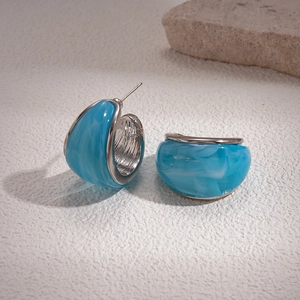 Detail of blue marble resin C-shaped hoop earrings on white stone surface