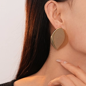 Close-up of a large golden comb-shaped metal earring worn by a model in soft light