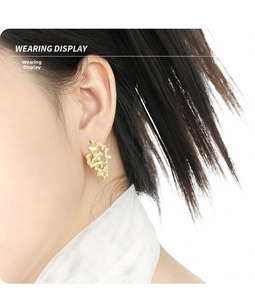 Close-up of gold irregular hollow stud earrings with textured lava finish on ear