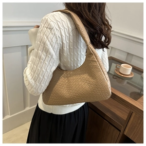 Detailed view of light brown crocodile pattern underarm bag worn by a model in a cafe