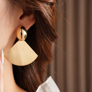 Close-up of golden fan-shaped earrings featuring brushed texture and oval studs