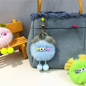 Close-up of blue monster plush keychain with googly eyes hanging on a denim bag strap