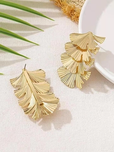 Detail der goldenen Ginkgo-Ohrringe mit strukturierten Schichten auf Naturstoffhintergrund