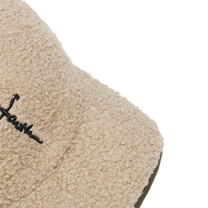 Dettaglio del tessuto agnellato beige con ricamo nero Youth sul cappello baseball