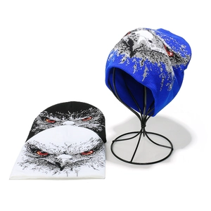 Three colors of knitted beanies with eagle prints shown on flat lay and metal stand