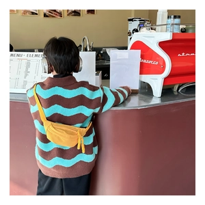 Yellow nylon kids chest bag styled with a wavy knit sweater in a cozy cafe setting