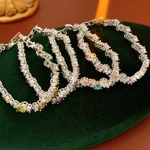 Detailed close-up of multi-colored zircon tennis bracelets on a dark green velvet display cushion