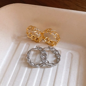 Close-up of gold and silver cuban link hoop earrings with zircon accents on a tray