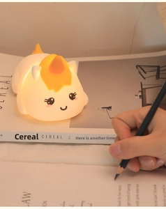 Close-up of a soft unicorn silicone lamp glowing warm yellow on a cozy desk setting