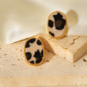 Macro detail of oval 18K gold earrings with leopard print inlay on beige textured stone