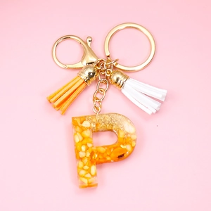 Macro view of golden letter P resin keychain with orange stone chips and colorful tassels