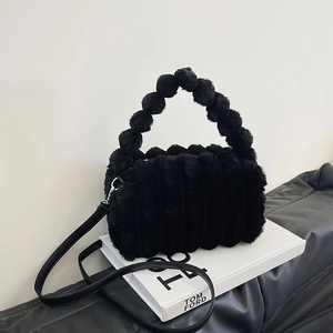 Plush faux fur handbag in black with beaded handle and leather strap on a designer book