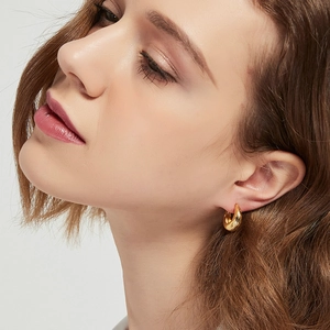 Close-up of a model wearing thick gold geometric hoop earrings on a clean white background