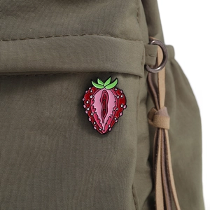 Detailed strawberry enamel pin badge pinned on a green canvas bag background