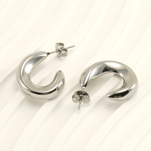 Close-up of thick silver C-shaped stainless steel earrings on a white textured background