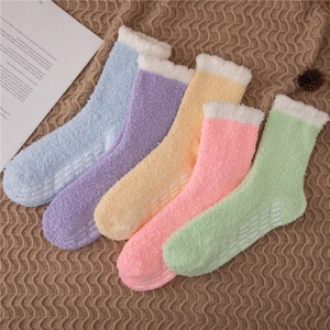 Close-up of colorful coral fleece fuzzy socks with anti-slip rubber grips on a blanket