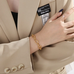 Polished gold link bracelet with knot design worn by model on beige suit jacket