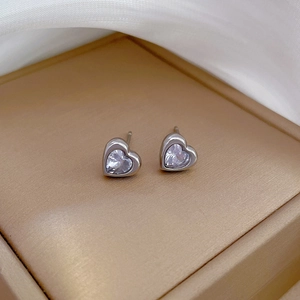 Macro shot of silver heart studs with clear zircon stones on champagne jewelry box