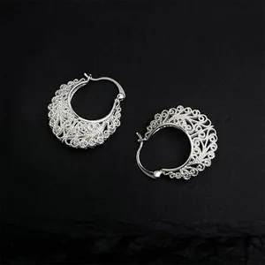 Ethnic style hollow lace silver hoop earrings displayed on a dark textured rock background