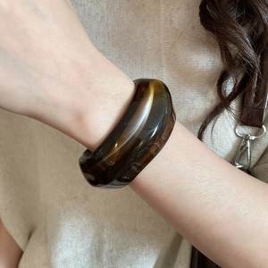 Close-up of translucent amber acrylic wide cuff bracelet on wrist with knitwear