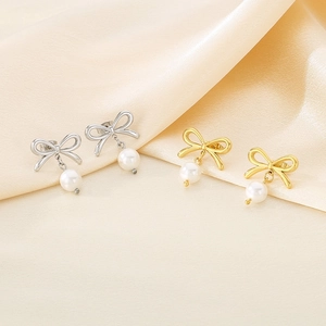 Detailed view of bow knot pearl earrings in gold and silver finish on silk fabric