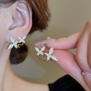 Detailed close-up of a delicate butterfly stud earring with white pearl finish