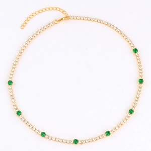 Close-up of gold tennis necklace featuring white cubic zirconia and green round gemstones