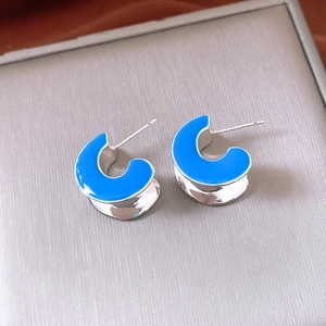 Detailed close-up of C-shaped earrings with bright blue enamel on silver metal base