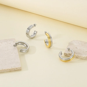 Polished silver and two-tone gold C-shaped hoop earrings on natural stone textures