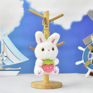 Detailed view of a cute white plush bunny keychain holding a strawberry on a stand
