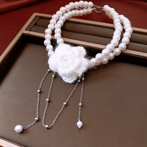 Detail of double-layer pearl necklace with a knitted white flower and silver chain tassels