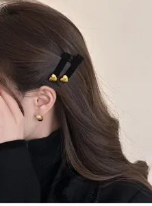 Dettaglio di piccole clip per capelli in velluto nero con cuori dorati su modella