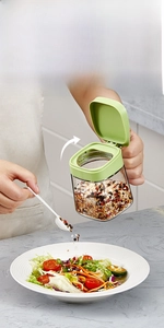 Detail of green glass spice jar with one-hand opening lid and spoon for salt and pepper