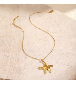 Close-up of golden starfish pendant necklace on textured beige stone surface