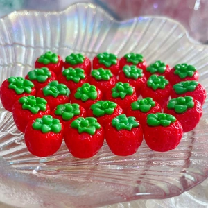 Dettaglio di ciondoli a fragola in resina rossa con foglie verdi in un vassoio di vetro
