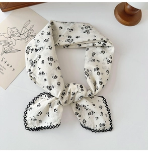 Detail of white cotton linen scarf featuring black floral prints and delicate lace trim