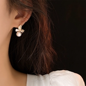 Close-up of gold-plated bow pearl earrings with zircon inlay worn by a fashion model