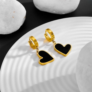 Détail macro des boucles d'oreilles dorées avec cœurs noirs sur un plateau blanc
