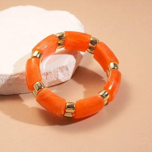 Detail of orange resin and gold metal chunky chain bracelet on white stone