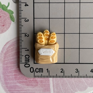 Close-up of miniature resin baguette in paper bag with yummy text and ruler for scale