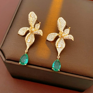 Close-up of gold flower earrings with pavé crystals and green teardrop gemstone drops