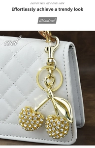 Detail of crystal cherry keychain with gold metal clasp on a white quilted handbag