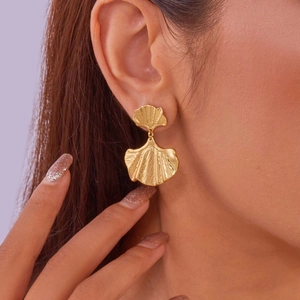Detail view of a 18K gold ginkgo leaf stud earring worn by a model on purple background