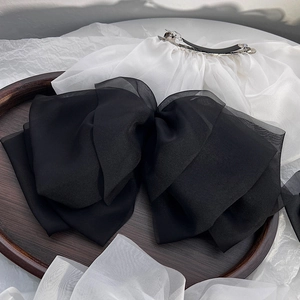 Detail of a large black chiffon bow hair clip on a wooden tray with elegant white fabric