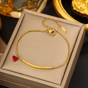 Detailed close-up of a gold heart charm bracelet with red crystal on a jewelry box