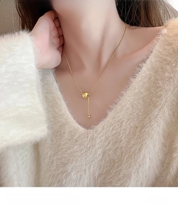 Detailed view of a gold ball pendant necklace on a cozy white sweater background