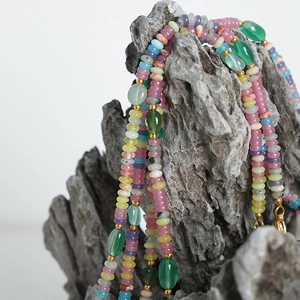 Collier artisanal en agate verte avec perles dorées suspendu sur une roche naturelle