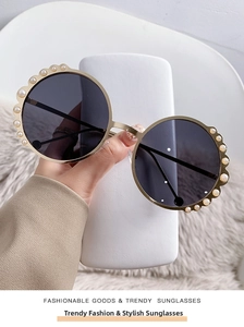 Detail of round frame sunglasses with pearl accents and gold metal temples on plush
